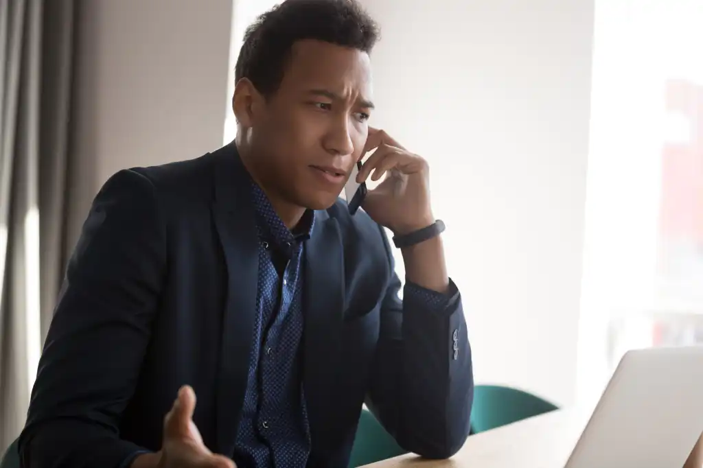 Angry stressed businessman disputing on phone with partner. Outraged african american manager, lawyer, banker, consultant or real estate agent listening bad news from client at office.
