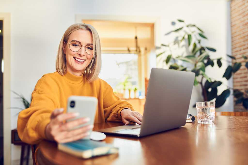 mature woman on phone loking at laptop