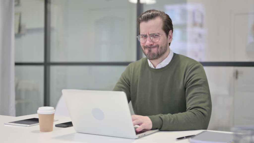 Young Businessman Shaking Head as No while using Laptop in Office