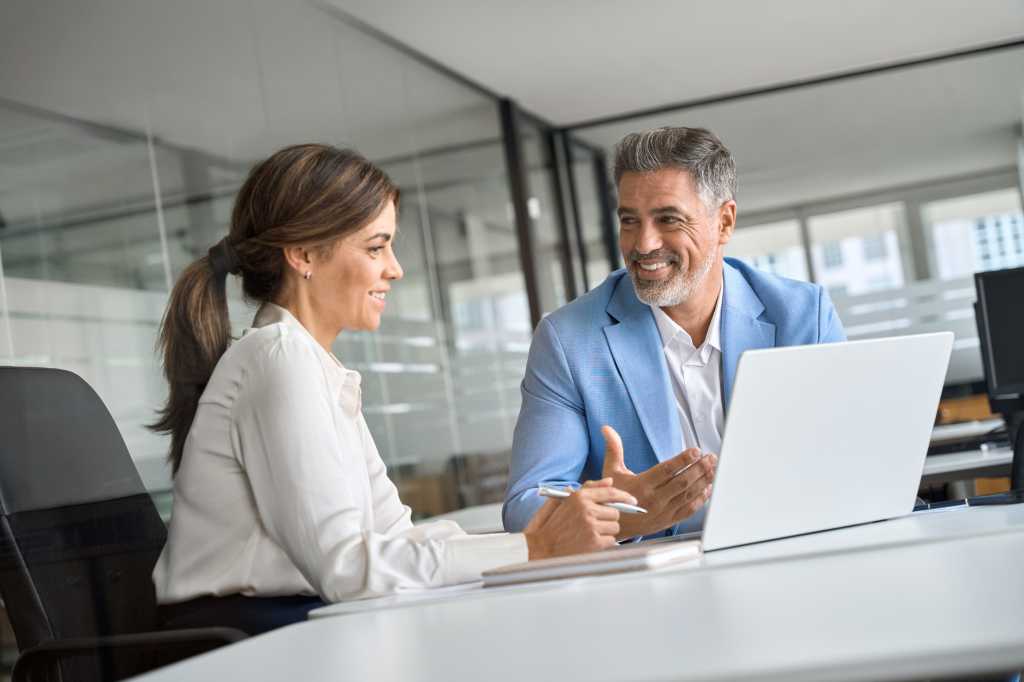 Professional bank manager consulting company client on financial taxes. Two middle aged professional executives team business people working together on laptop computer at office corporate meeting.